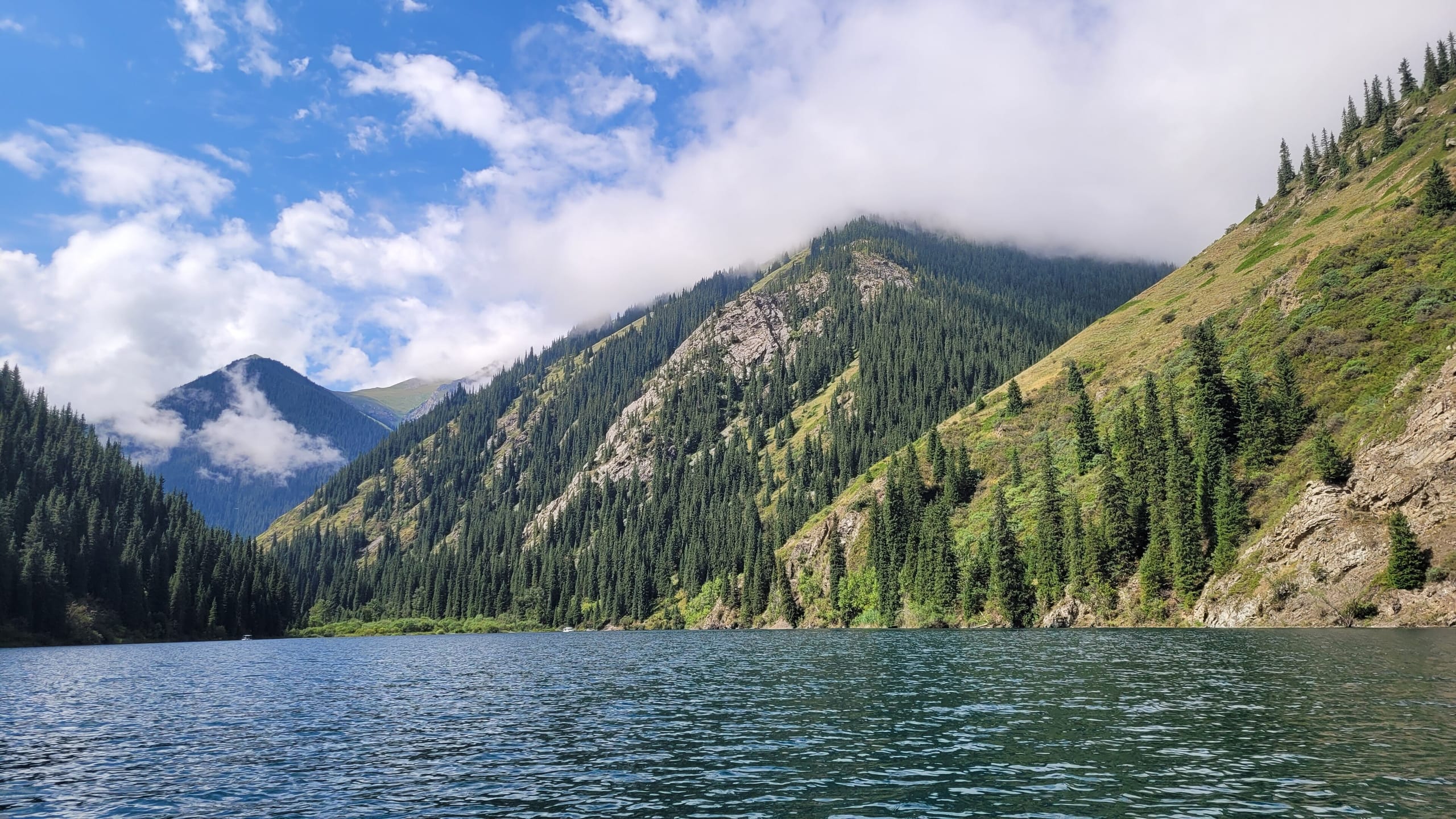 Forested alpine valley and blue lake at Kolsai Lakes in Kazakhstan under a bright sky