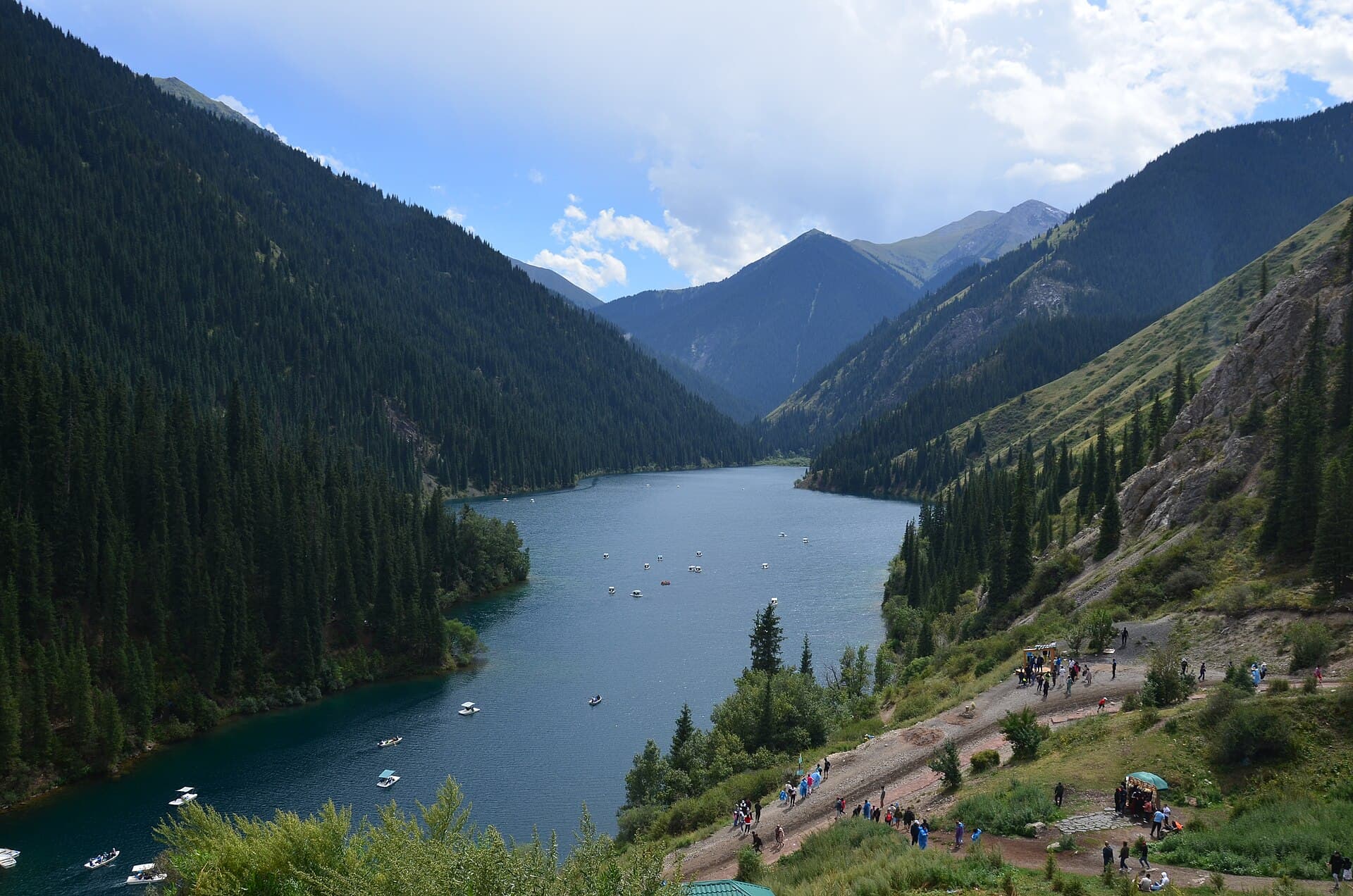 Visitors and pedal boats beside a deep blue mountain lake in the Kolsai Lakes national park